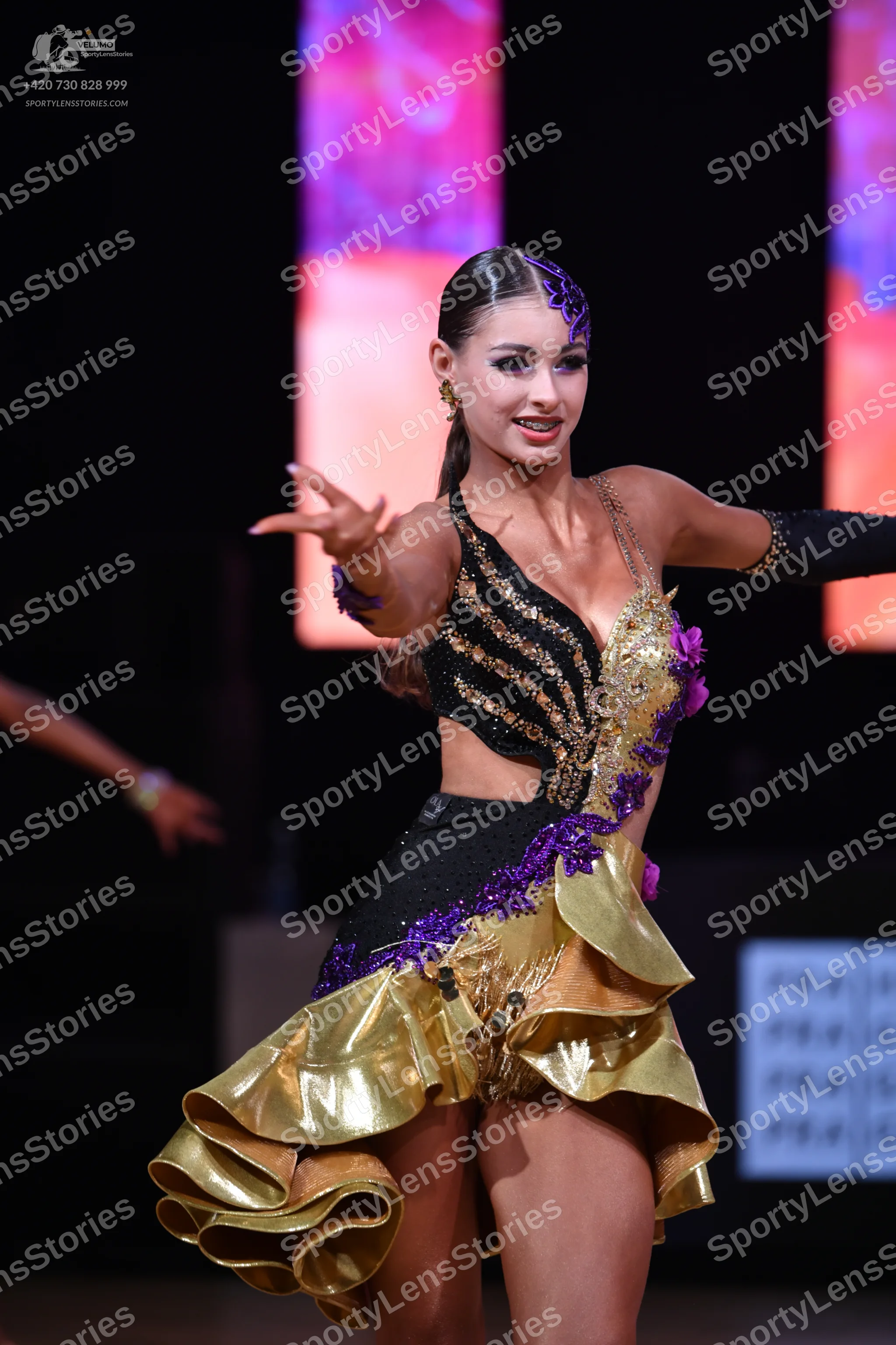 Dancesport competitor: Female dancer: black, gold, and purple latin dress with sequin stripes, purple l