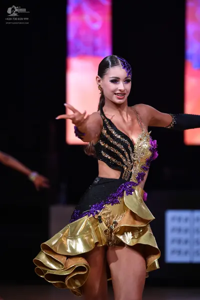 Dancesport competitor: Female dancer: black, gold, and purple latin dress with sequin stripes, purple l