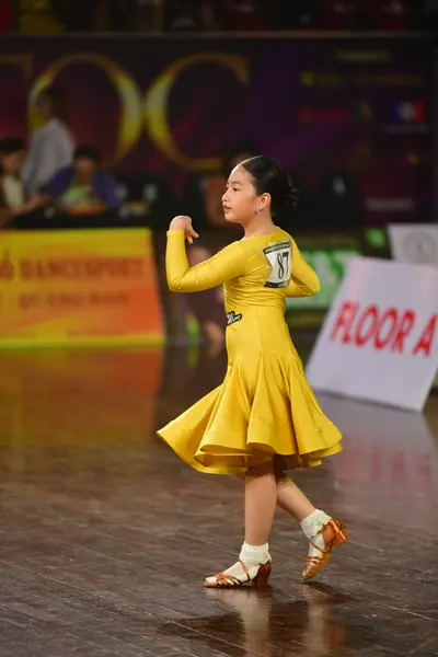 Dancesport competitor: Female dancer: yellow latin dress with long sleeves and a flared skirt; cream-co