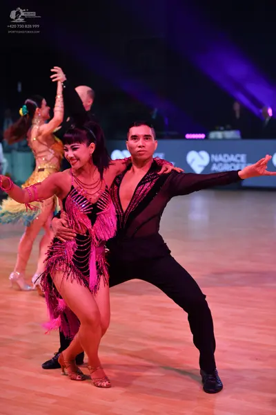 Dancesport competitor: Foreground female dancer: pink latin dress with sequins and fringe