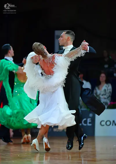 Dancesport competitor: Male dancer in foreground: black ballroom suit with a white shirt and white bow 