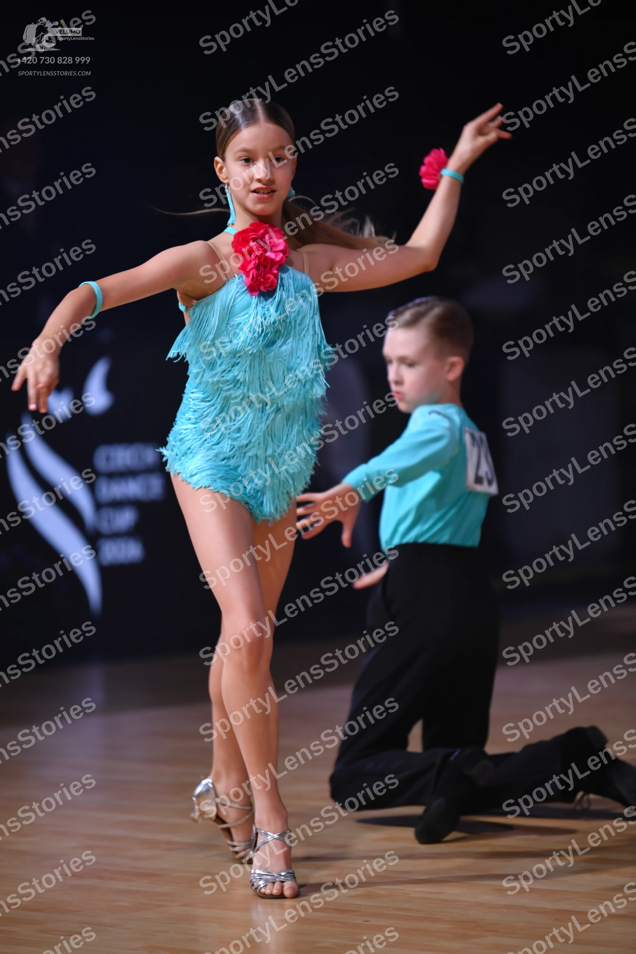 Dancesport competitor: Female dancer: turquoise latin dress with fringe texture and a pink flower acces