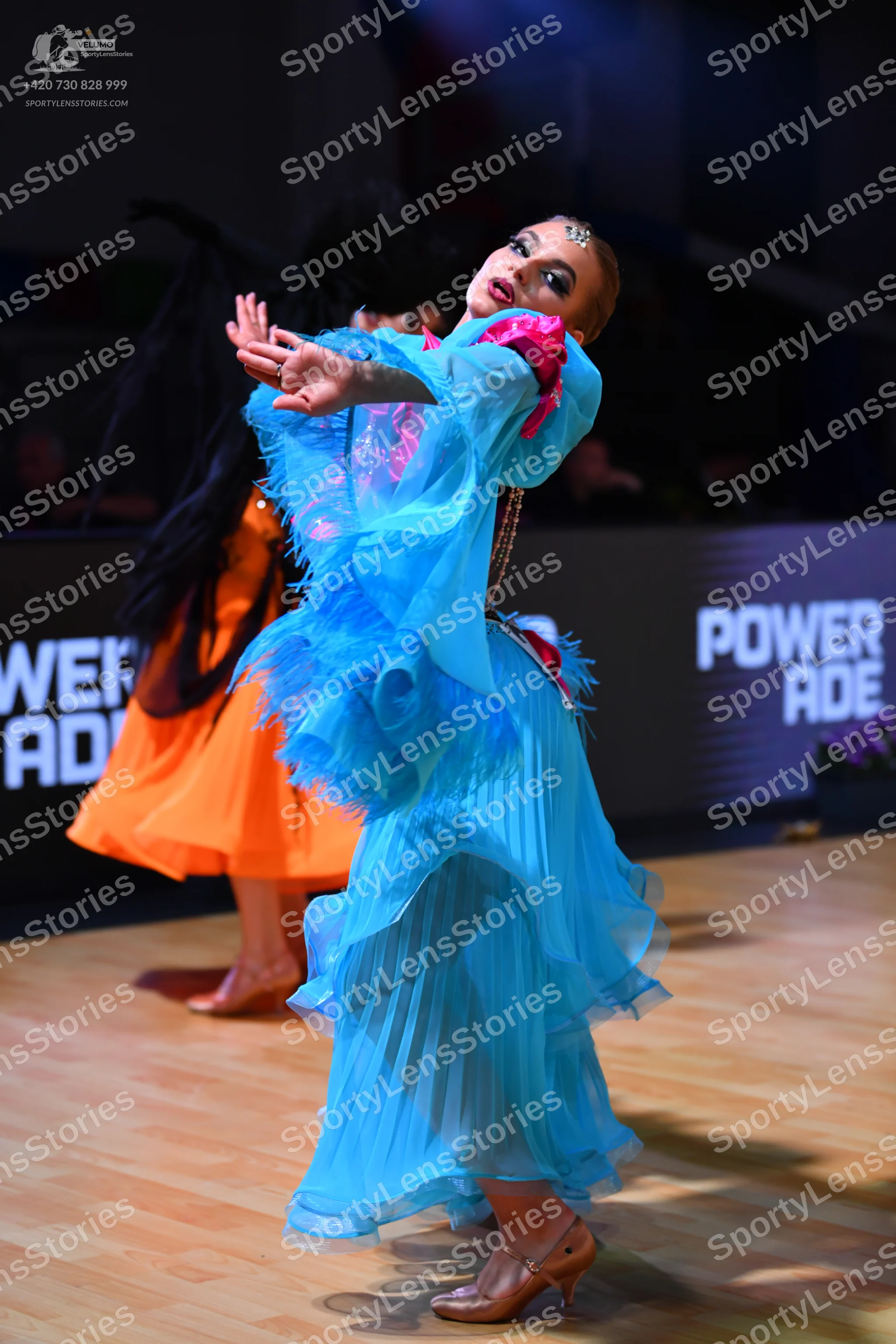 Dancesport competitor: Female dancer in foreground: light blue flowing dress with layered ruffles and p