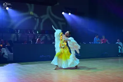 Dancesport competitor: Female dancer: white and yellow costume featuring voluminous, white, furry or fe