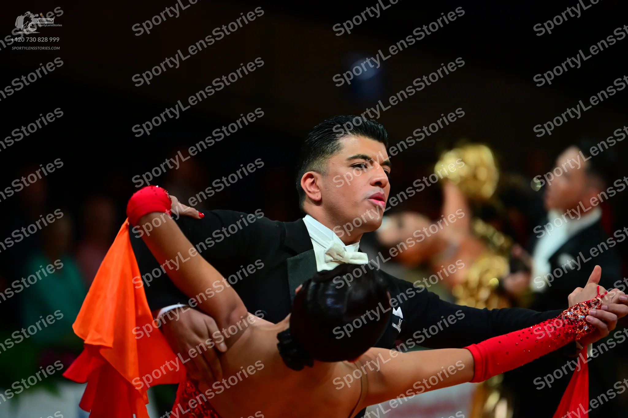 Dancesport competitor: Male dancer in foreground: black tuxedo with satin lapels, white shirt, and whit