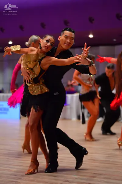 Dancesport competitor: Main female dancer: gold sequin bodice, black fringe skirt, and a gold cuff acce