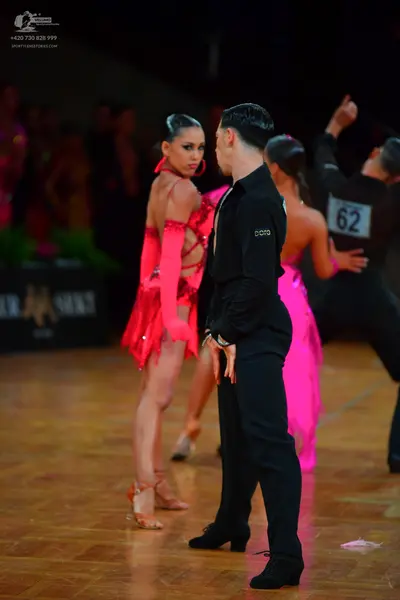 Dancesport competitor #62: Female dancer in foreground: bright red/pink latin dress with sequins and fringe