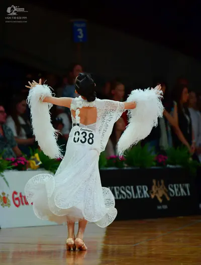 Dancesport competitor: Female dancer: white lace dress with large white feather accents on the sleeves 