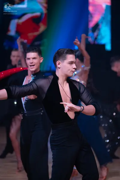 Dancesport competitor: Male dancer in foreground: black long-sleeved top with sheer mesh panels on the 