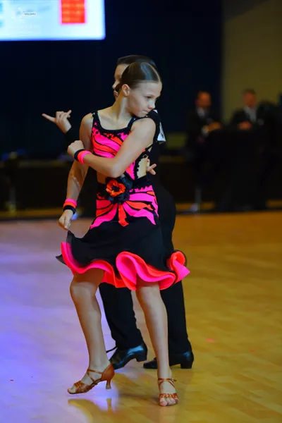 Dancesport competitor: Female dancer: black Latin dance dress with bright pink patterns and a ruffled p
