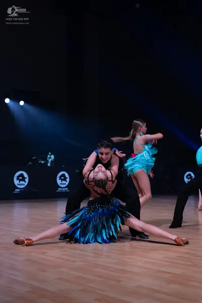 Dancesport competitor: Female dancer in foreground: dark blue and black Latin dance dress with a skirt 