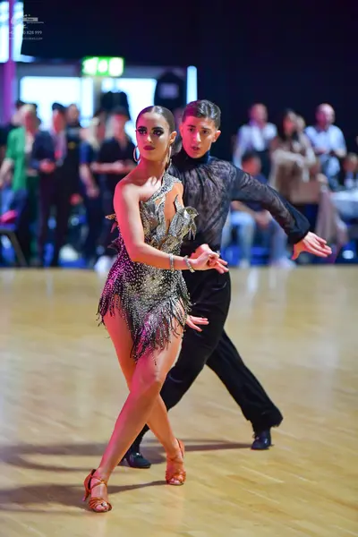 Dancesport competitor: Female dancer: metallic gold one-shoulder Latin dress with sequins and fringe, h