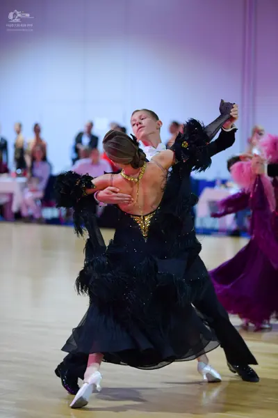 Dancesport competitor: Female dancer: black ballroom dress with a sequined bodice and feathered or frin