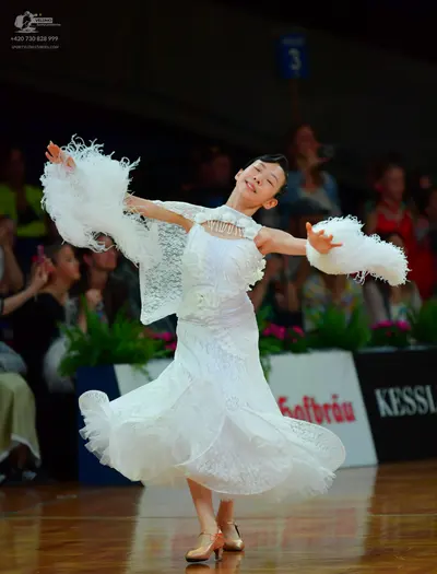 Dancesport competitor: Female dancer: white lace ballroom dress with large, white feathery trim on the 