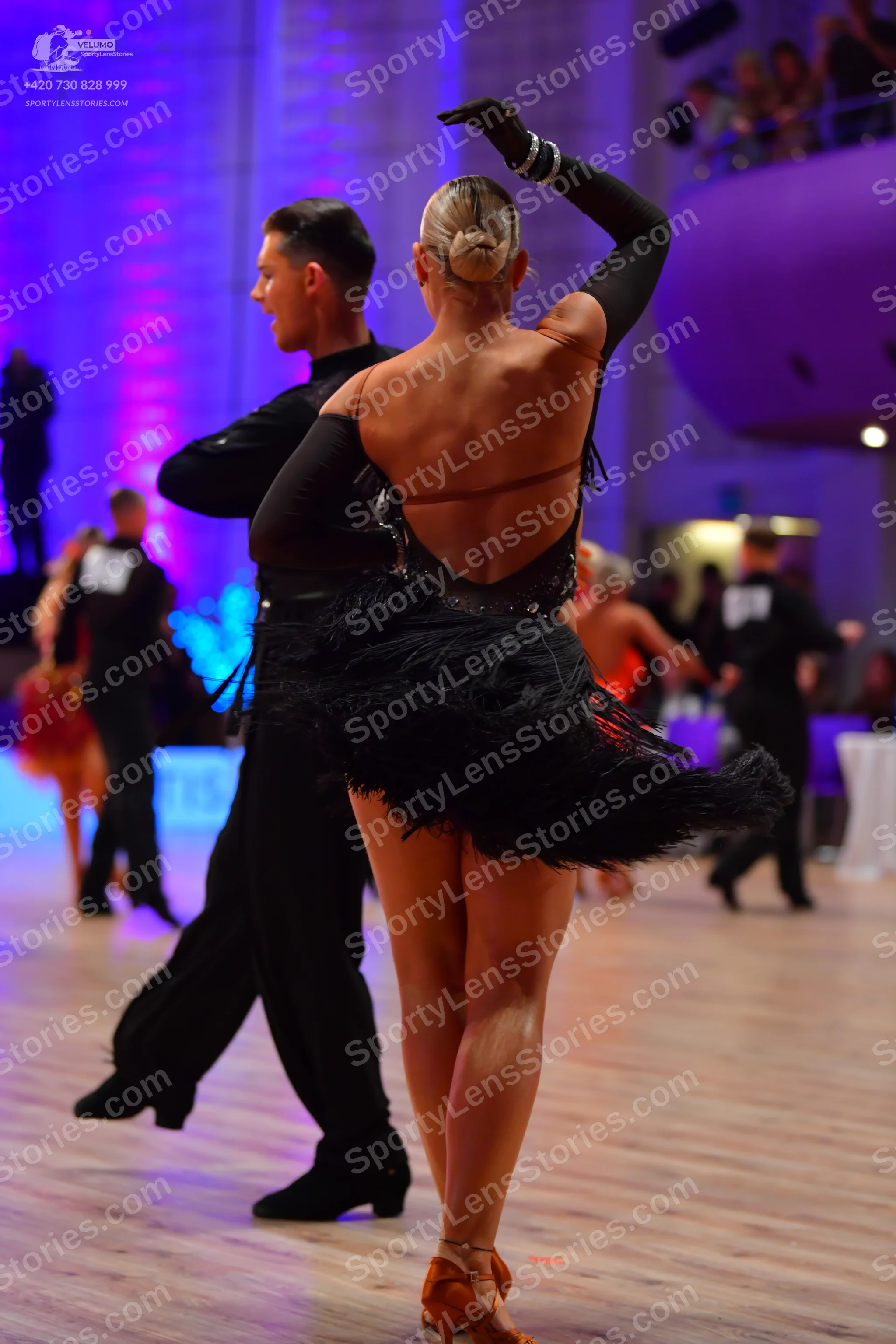 Dancesport competitor: Foreground female dancer: black Latin dress with long sleeves, an open back, and