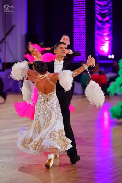Dancesport competitor: Female dancer: white ballroom dress with gold sequin patterns and large white fl