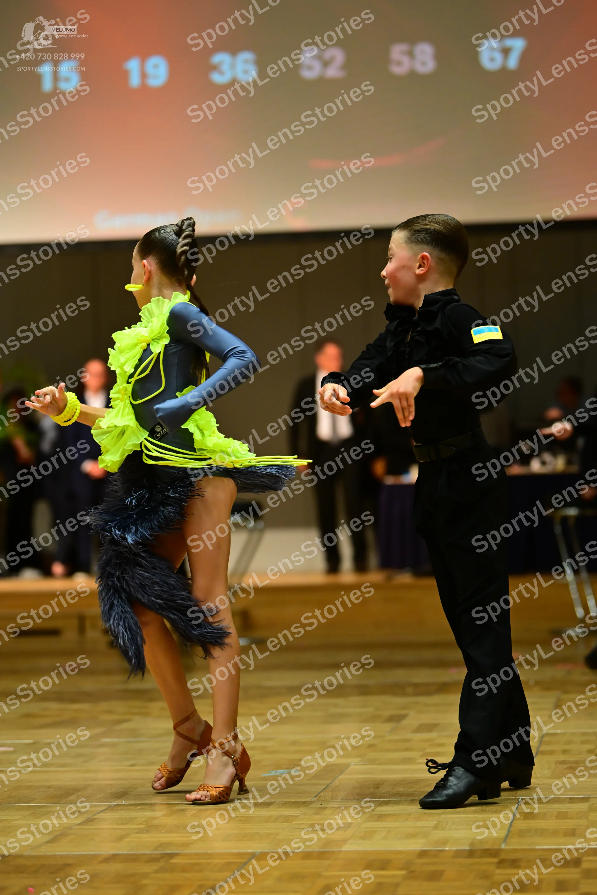 Dancesport competitor: Female dancer: dark blue Latin dress with bright neon yellow ruffles and a neon