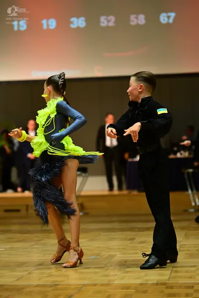 Dancesport competitor: Female dancer: dark blue Latin dress with bright neon yellow ruffles and a neon 