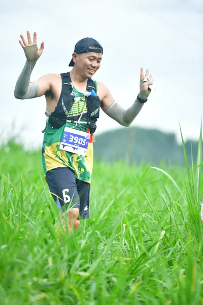 Marathon runner #3905: Runner 1: green and black tank top, dark shorts, black arm sleeves, black cap, a