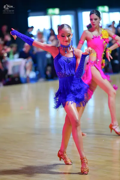 Dancesport competitor: Female dancer in foreground: blue Latin dress with fringe and sequins, matching 