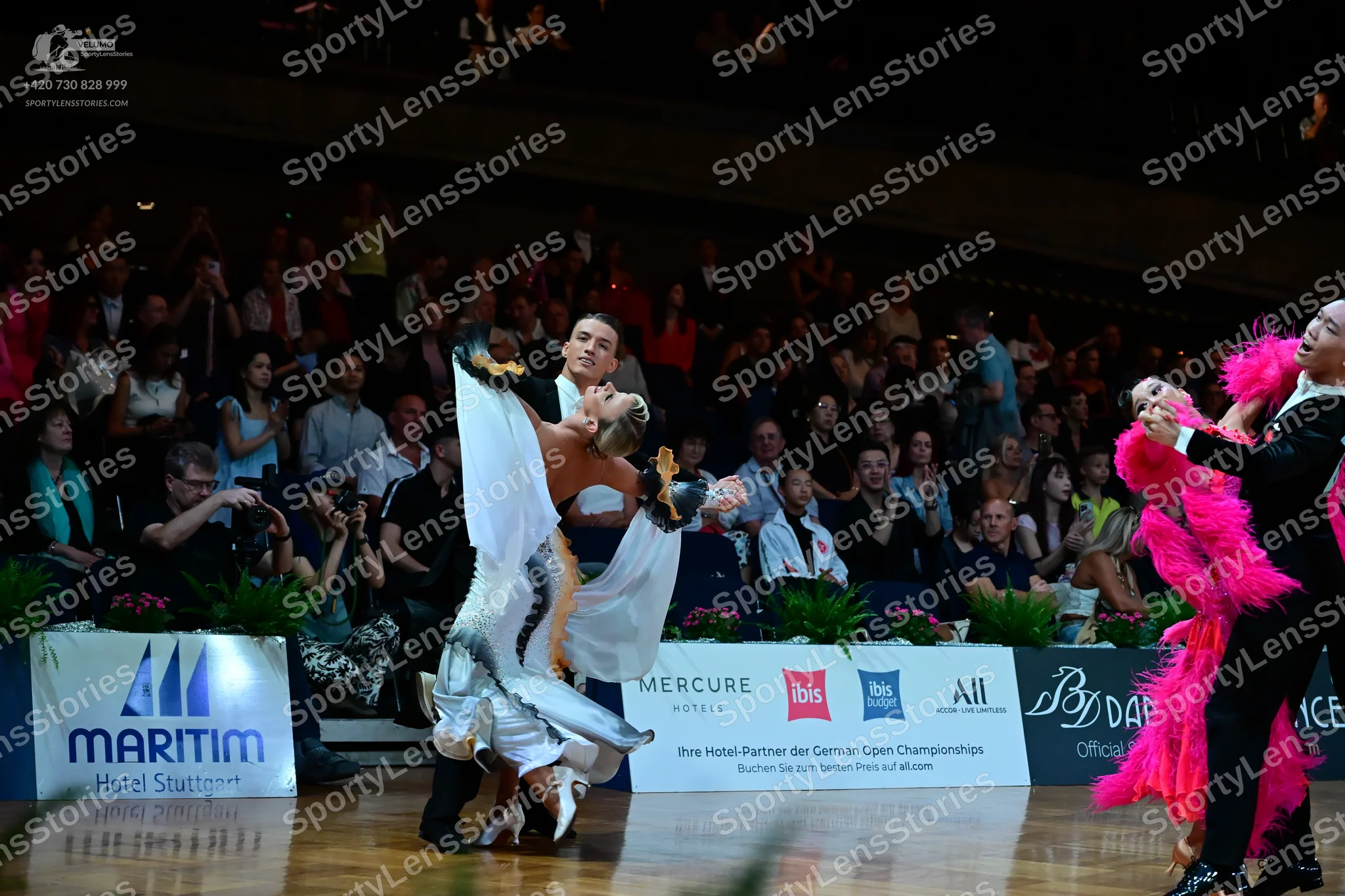 Dancesport competitor: Male dancer 1: dark suit; Female dancer 1: silver/white latin dance dress with l