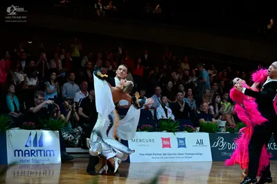 Dancesport competitor: Male dancer 1: dark suit; Female dancer 1: silver/white latin dance dress with l