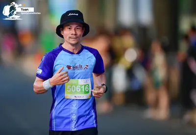 Marathon runner #50616: Runner 1: blue and purple jersey, black shorts, black bucket hat, white wristban