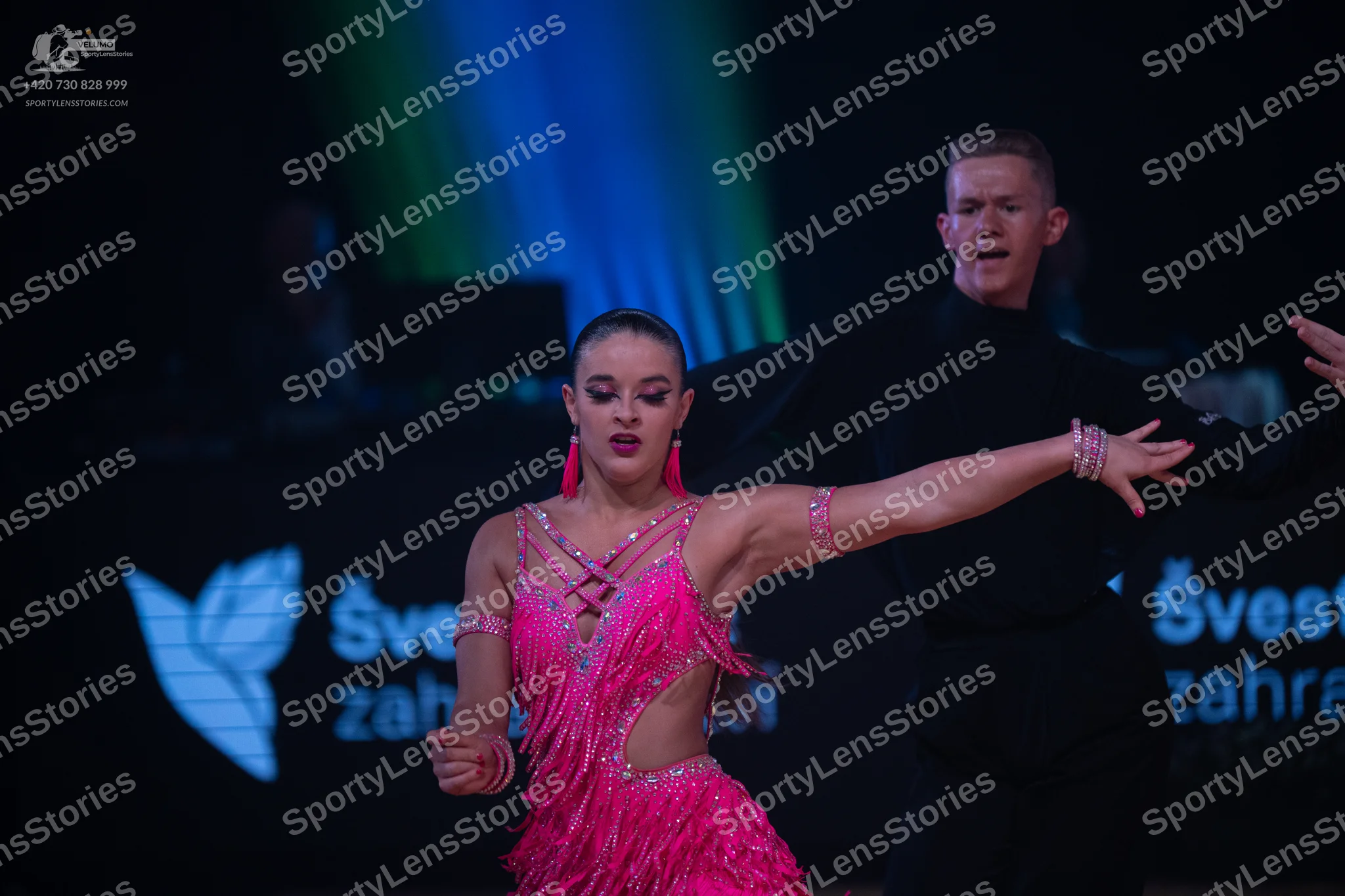 Dancesport competitor: Female dancer: pink latin dress with sequins and fringe, pink earrings, and brac