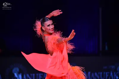 Dancesport competitor: Female dancer: bright orange Latin dress with feather-like fringe on the sleeves