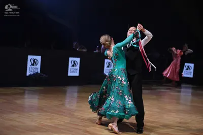 Dancesport competitor: Female dancer in foreground: teal long-sleeved ballroom dress with a floral patt