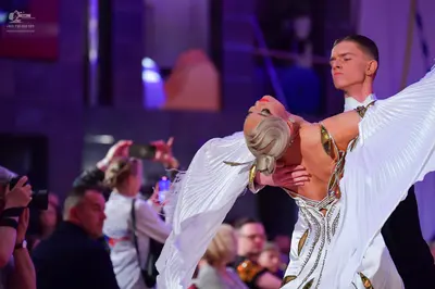Dancesport competitor: Female dancer: white ballroom dress with large, flowing, pleated white fabric sl