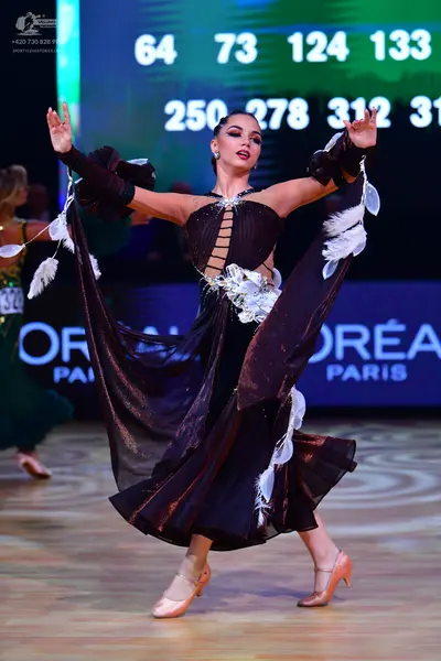 Dancesport competitor: Main dancer: dark brown or black ballroom dress with metallic shimmer, featuring