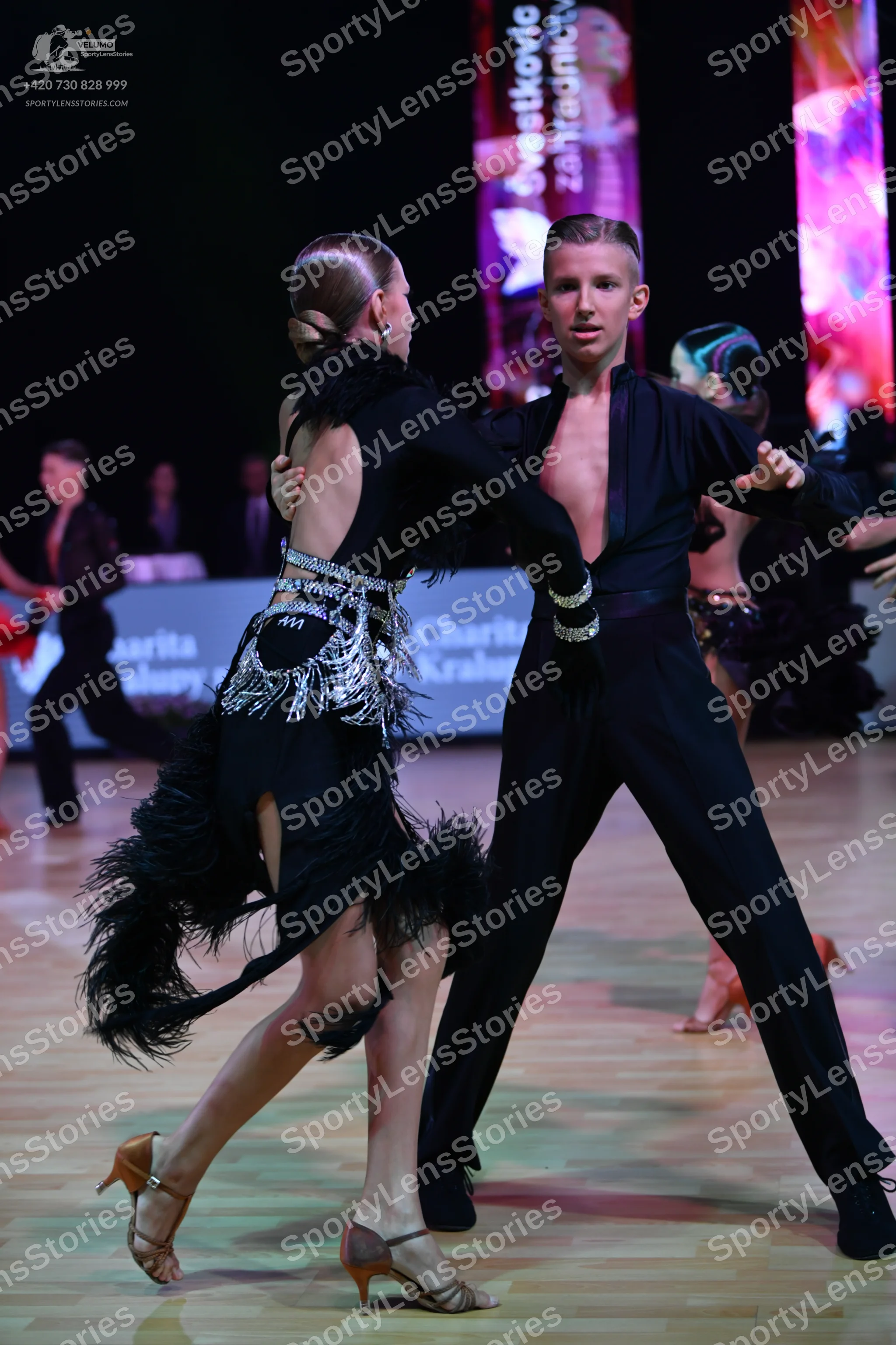Dancesport competitor: Foreground female dancer: black long-sleeve latin dress with silver sequin embel