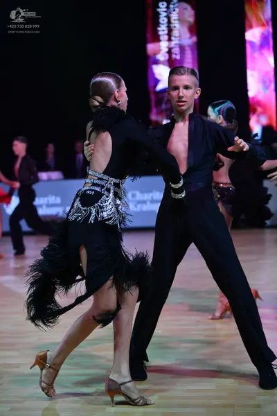 Dancesport competitor: Foreground female dancer: black long-sleeve latin dress with silver sequin embel