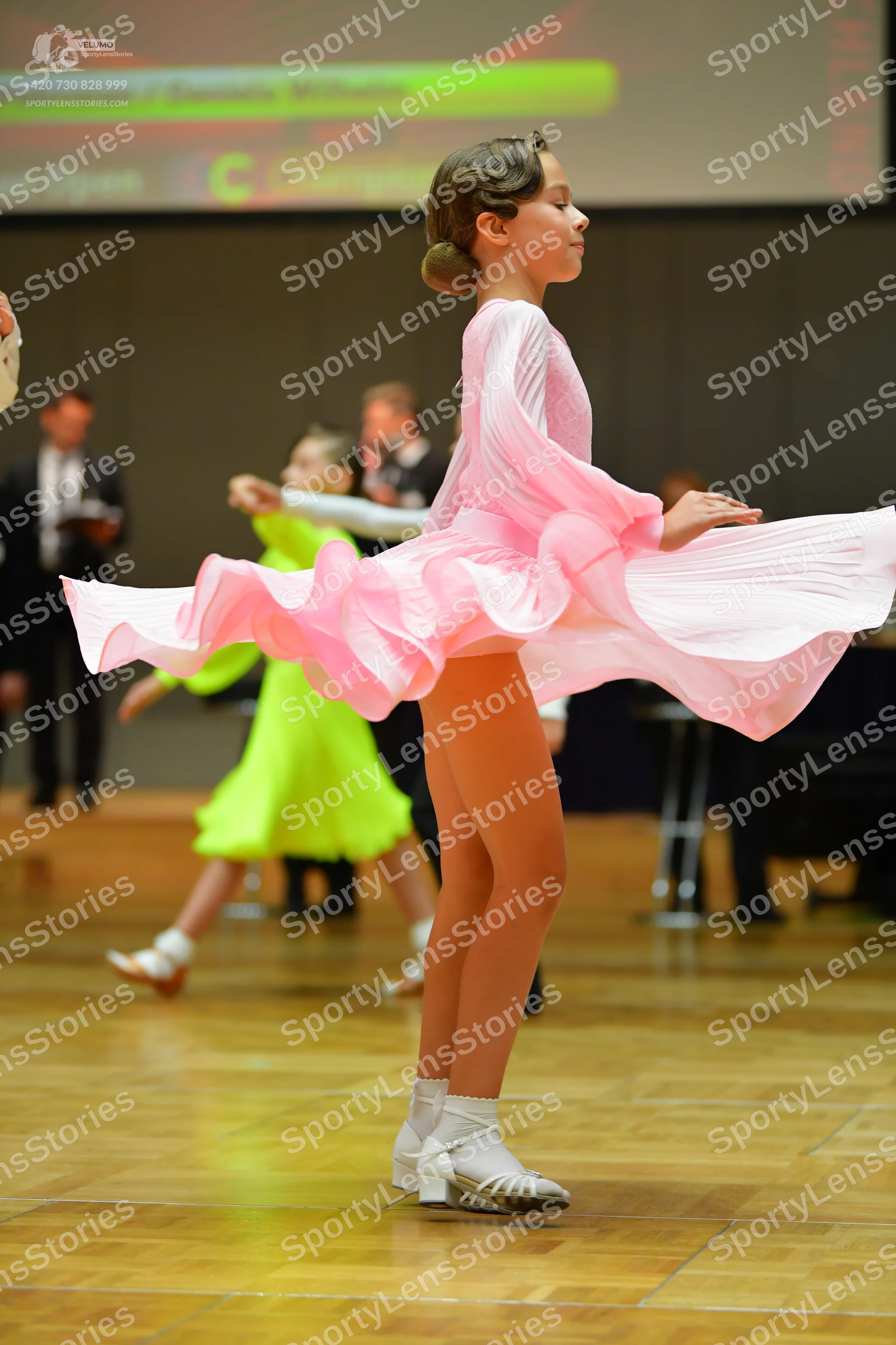 Dancesport competitor: Female dancer in foreground: light pink latin dress with long sleeves and a volu