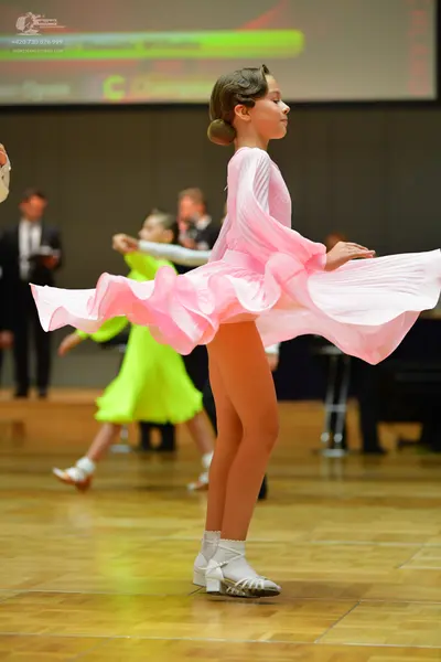 Dancesport competitor: Female dancer in foreground: light pink latin dress with long sleeves and a volu