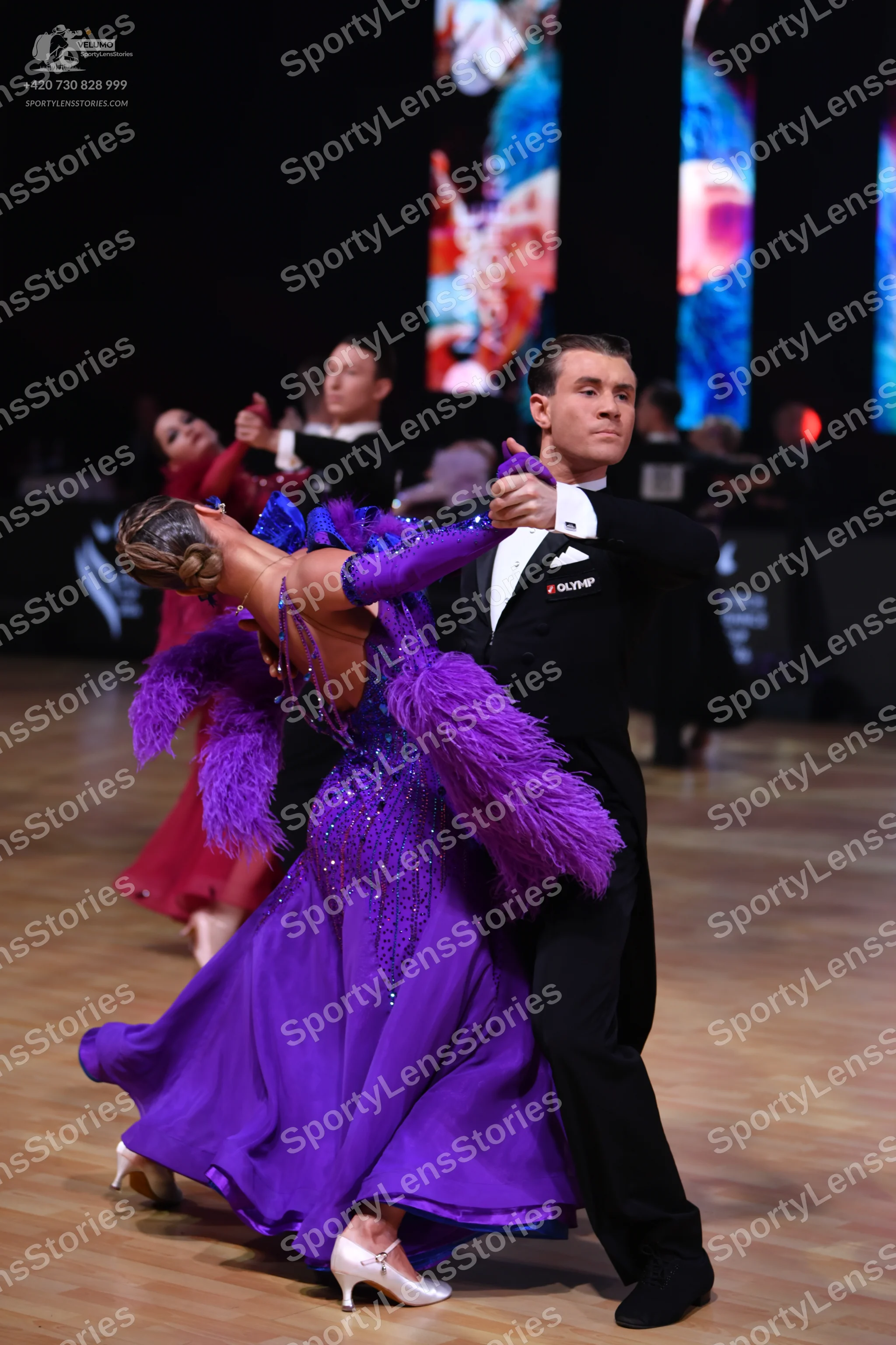 Dancesport competitor: Female dancer: purple ballgown with large purple feather trim on the shoulders a