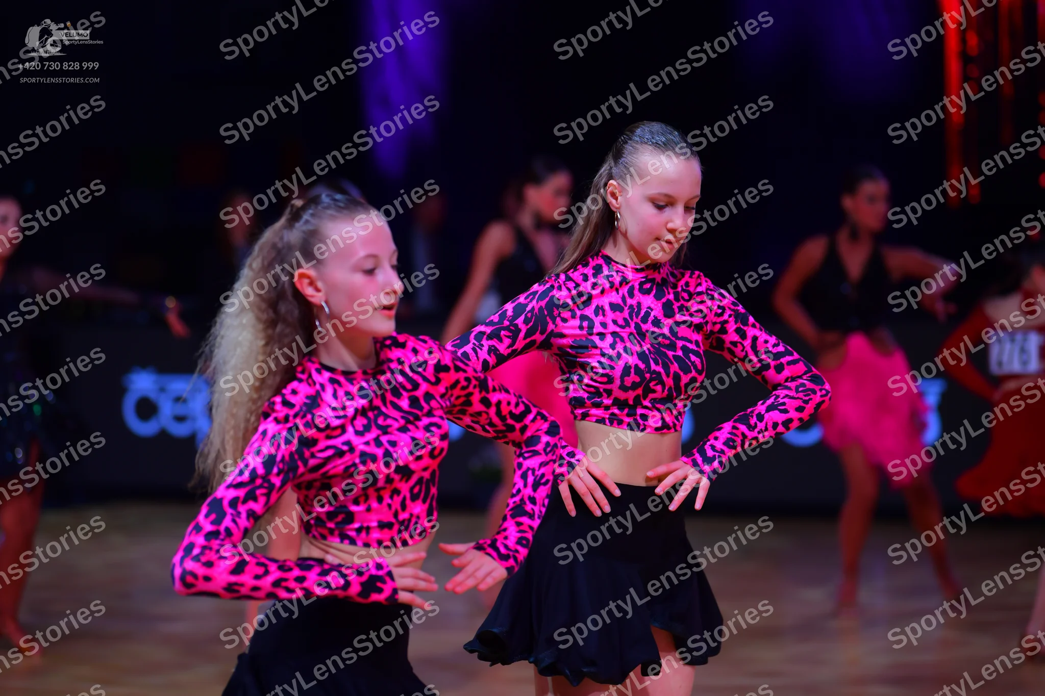 Dancesport competitor: Two foreground dancers: matching pink and black leopard print long-sleeved crop