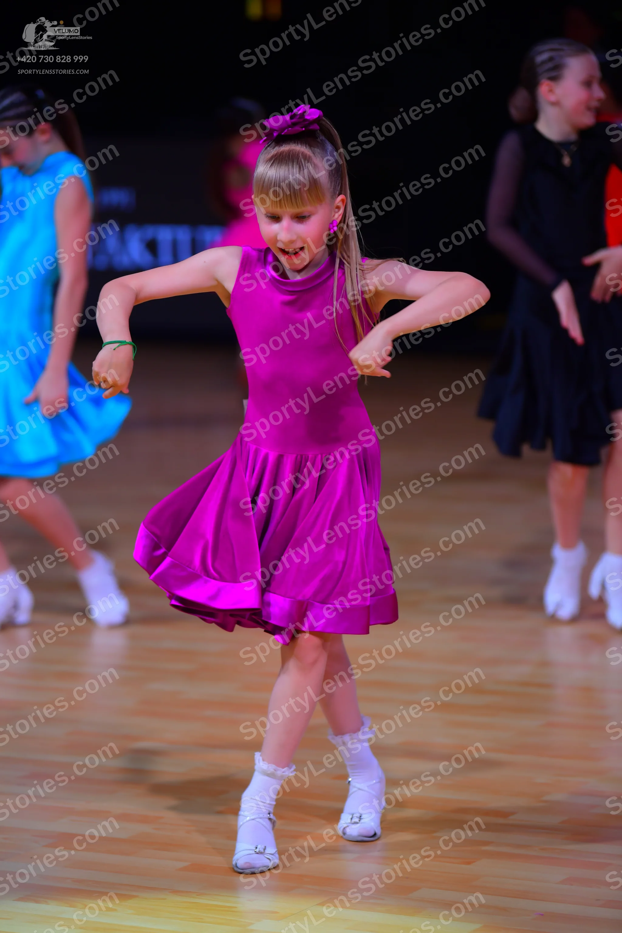 Dancesport competitor: Female dancer in foreground: magenta sleeveless dress with a high neckline and f