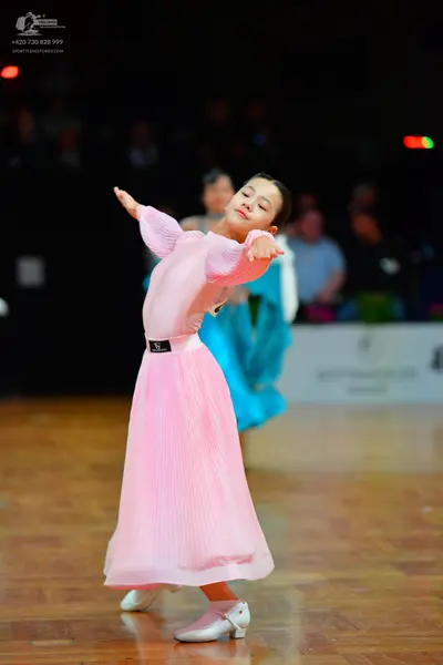 Dancesport competitor: Female dancer in foreground: light pink, long-sleeved ballgown with a smooth, sl