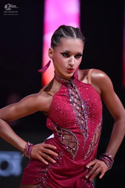 Dancesport competitor: Female dancer: deep red Latin dress with sequins and crystals, featuring a criss