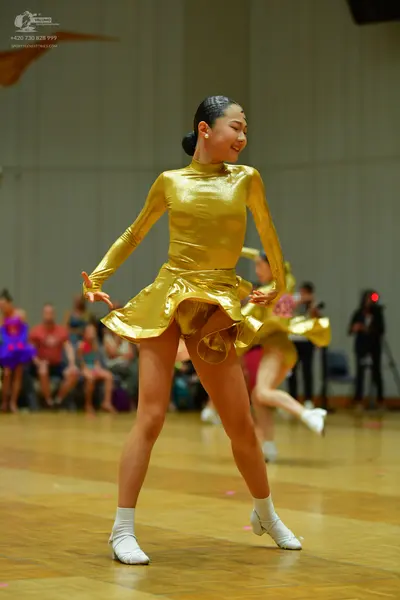 Dancesport competitor: Female dancer: gold metallic long-sleeved Latin dress with a short flared skirt,
