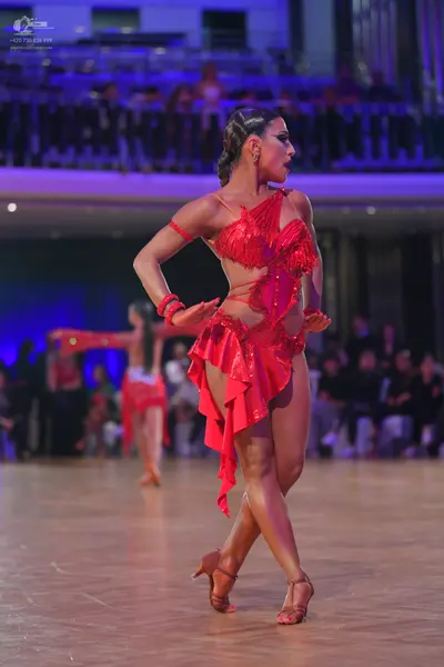 Dancesport competitor: Female dancer in foreground: red Latin dress with sequins and fringe, red armban