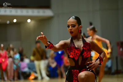 Dancesport competitor: Female dancer in foreground: red and black Latin dance dress with sequin embelli