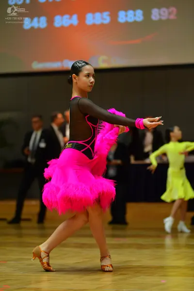 Dancesport competitor: Female dancer in foreground: bright pink and black Latin dress with a voluminous