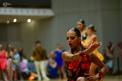 Dancesport competitor: Primary female dancer: dark Latin dance costume with red and black geometric pat