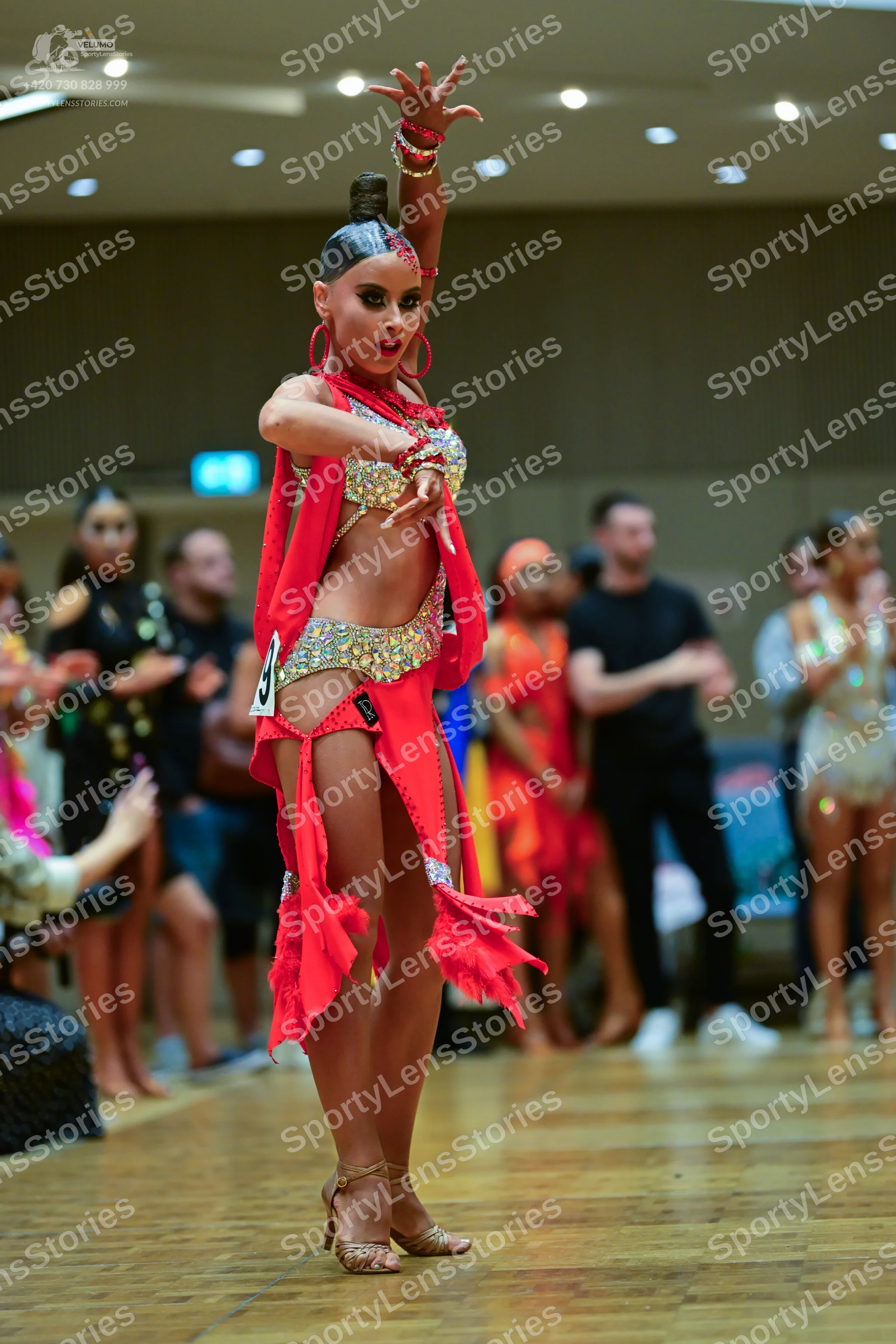Dancesport competitor: Female dancer in foreground: red Latin dress with a sequin-embellished bodice, m