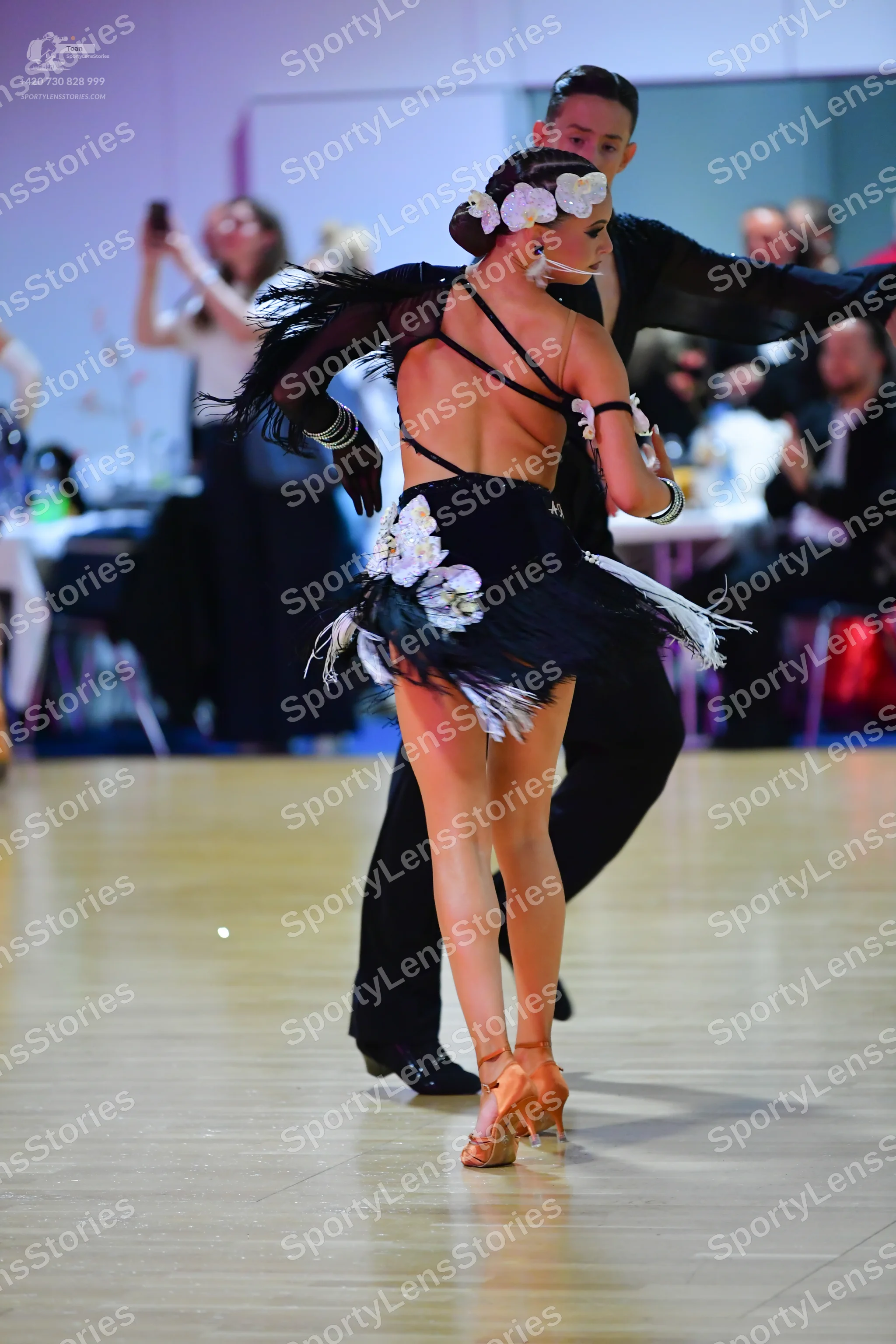 Dancesport competitor: Female dancer: black Latin dress with white floral/feather embellishments and wh