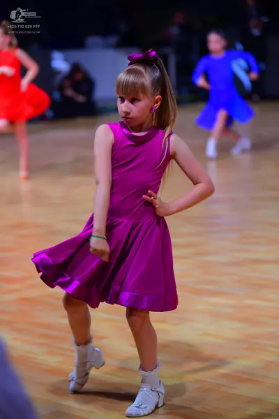 Dancesport competitor: Female dancer in foreground: magenta sleeveless latin dress with a flared skirt,