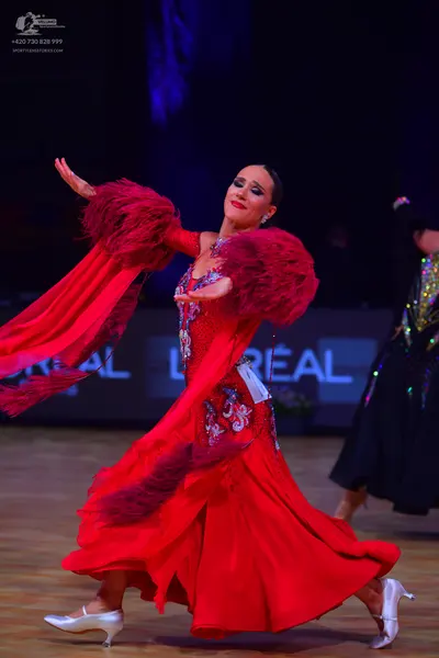 Dancesport competitor: Female dancer in foreground: red dance dress with long sleeves featuring large r